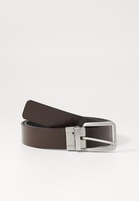 Bruine leren riem met een slank, plat ontwerp, voorzien van een zilveren metalen gesp met gegraveerde branding. Zachte textuur en minimale details.