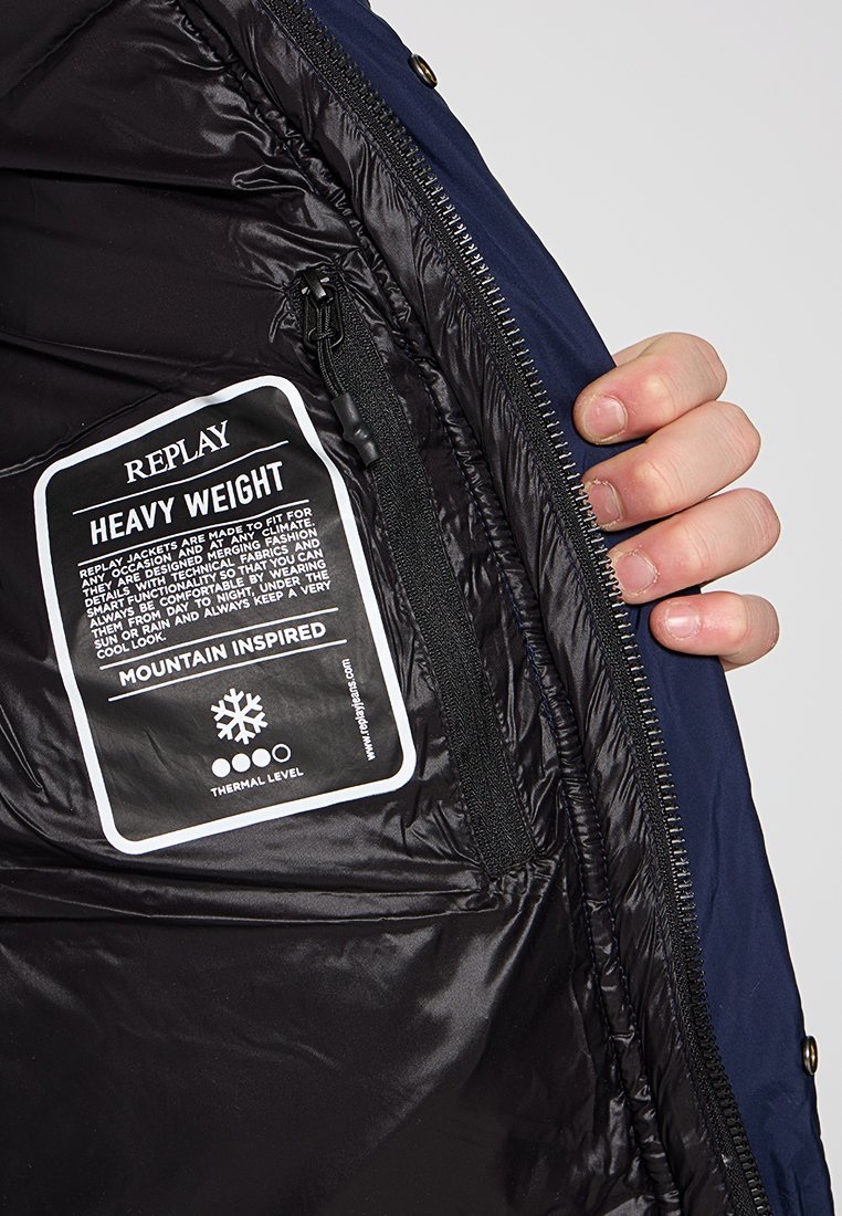 Czarna tkanina wnętrza ciężkiej kurtki z białą metką. Metka zawiera nazwę marki "REPLAY" oraz instrukcje dotyczące pielęgnacji.