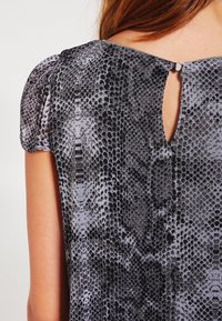 Grå och svart ormtryckt topp med korta puffärmar, med en nyckelhålsdetalj på baksidan och slätt, texturerat tyg.