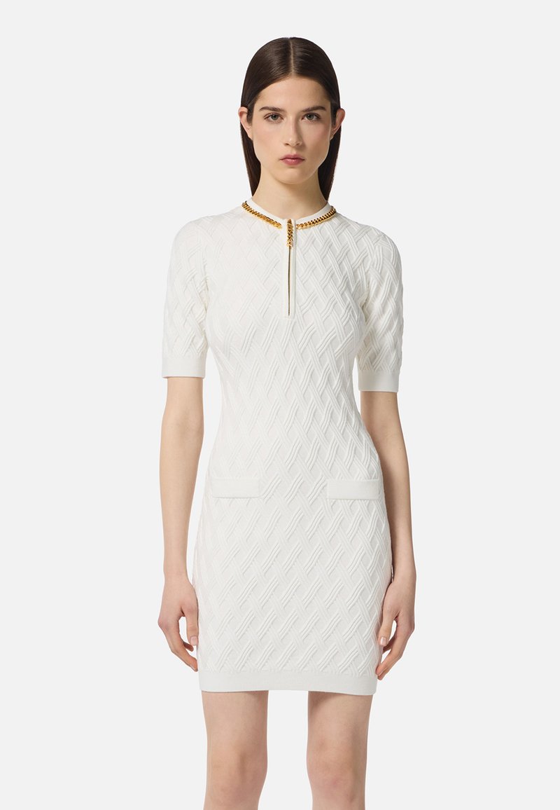 Abito bianco a maglia con un motivo a diamante testurizzato, maniche corte, due tasche frontali e un colletto accentato in oro con una cerniera centrale.