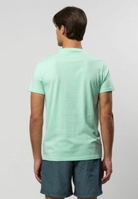 Mentolově zelené tričko s krátkým rukávem, kulatým výstřihem, z bavlněné látky, přiléhavého střihu, hladké textury, v kombinaci s modrými krátkými kalhotami s vzorem.