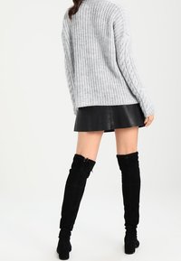 Grau gestrickter Pullover mit Kabelmuster, kombiniert mit einem schwarzen, kunstledernen Minirock und knielangen schwarzen Wildlederstiefeln.