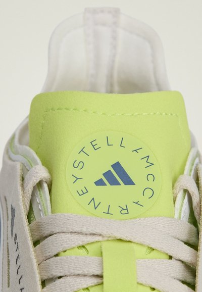 Light gray sneaker with a neon green suede tongue and logo patch. Features beige laces and stitching, smooth texture, and minimalist design.