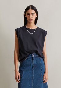 Black cotton sleeveless top with a round neck, paired with a blue denim skirt featuring a front button closure and back slit.