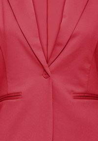 Gros plan sur un blazer rouge avec une fermeture à un bouton, des revers à encoche et deux poches horizontales à l'avant.