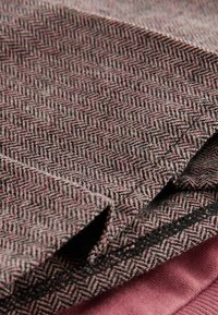 Textiles que presentan un patrón de espiga en tonos de rosa y gris, con un acabado suave y texturizado. Se ven bordes de tela superpuestos.