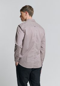 Langarmhemd in Hellbraun mit geometrischem Muster. Verfügt über einen klassischen Kragen, Knopfmanschetten und ein einzelnes Knopfdetail auf der Rückseite.