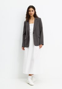 Grauer Blazer mit minimalistischer 디자인 über einem weißen trägerlosen Kleid. Kombiniert mit weißen Sneakers und bietet eine glatte Textur.
