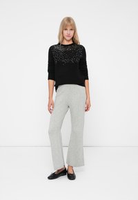 Maglione nero a maglia con ornamenti luccicanti sul collo, abbinato a pantaloni grigi a gamba larga e ballerine nere. Design semplice e moderno.