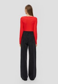 Rotes langärmliges Oberteil, kombiniert mit hochtaillierten, weit geschnittenen schwarzen Jeans. Glatter Stoff und minimale Nähdetails an den Jeans.