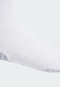 Calcetín deportivo blanco con textura acanalada y un sutil patrón gris en el puño. El material parece transpirable y elástico para mayor comodidad.