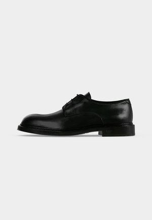 Chaussure habillée pour homme en cuir noir poli à lacets, avec un petit talon et un bout simple, présentée en profil sur fond blanc.