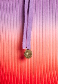 Gestreifter Farbverlauf-Stoff, der von Lila zu Rot übergeht, mit einem lila Zugband und einem goldenen, runden Emblem mit "Versace"-Markenlogo.