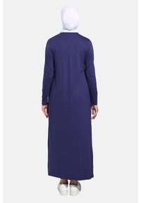 Dlouhé námořnické modré šaty z hladkého materiálu, s dlouhými rukávy a volným střihem, spárované s bílými teniskami. Jednoduchý design, bez vzorů.