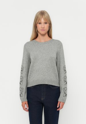 Grijze gebreide trui met lange mouwen, voorzien van zwarte bloemenborduursels op de mouwen, een ronde halslijn en een geribbelde zoom. Gecombineerd met donkere jeans.
