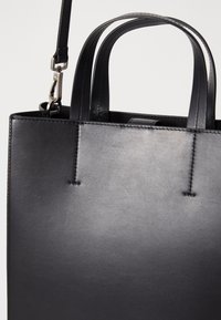 Geantă tote din piele neagră, cu formă structurată, cusături verticale, două mânere superioare și curea detașabilă. Textură elegantă și netedă, design minimal.