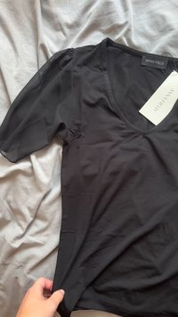 T-shirt preto com decote em V e mangas curtas em tule. Tecido suave, textura lisa. Etiqueta visível com a marca "ANNA FIELD".