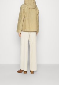 Světle béžová bunda s kapucí, s jemným leskem. V kombinaci s širokými krémovými manšestrovými kalhotami a hnědými koženými botami na podpatku.