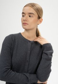 Dunkelgraue Strickjacke aus weichem Stoff, mit Rundhalsausschnitt, fünf Knopfverschluss und gerippten Bündchen. Glatte Textur mit minimaler Ausstattung.