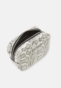 Příruční taška se stříbrnou hadí texturou, obdélníkového tvaru, se dvěma zipovými uzávěry a černým vnitřkem. Uvnitř se nachází branding Calvin Klein Jeans.