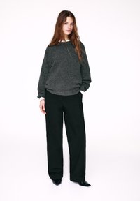 Maglione grigio in maglia con maniche lunghe, abbinato a pantaloni neri larghi. Il maglione presenta una scollatura rotonda; scarpe nere con punta completano l'outfit.