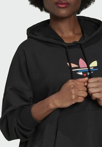 Felpa nera con cappuccio e un grande logo multicolore Adidas al centro. Caratterizzata da una vestibilità ampia, maniche lunghe e una tasca a marsupio frontale.