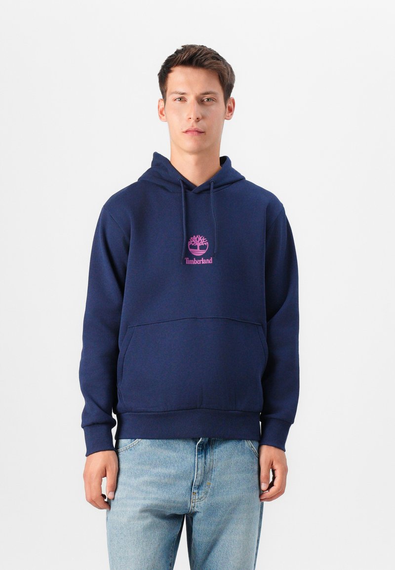 Námořnická modrá mikina s kapucí, s přední klokánkovou kapsou, žebrovanými manžetami a pasem. Na hrudi se nachází růžové logo Timberland. Materiál je směs bavlny.