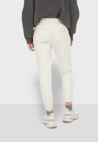 Jasno beżowe spodnie o kroju dopasowanym z elastycznym pasem, z wąską sylwetką i kieszeniami z tyłu, w połączeniu z białymi sneakersami i ciemnoszarym swetrem.