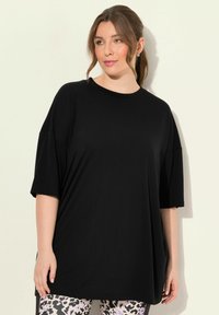 T-shirt nera oversize realizzata in tessuto morbido, con scollatura rotonda e maniche corte, abbinata a leggings con fantasia.