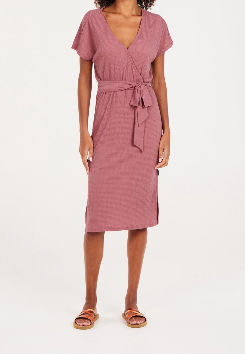 Robe portefeuille rose-rosée à manches courtes, tissu texturé, taille nouée, et fentes latérales, associée à des sandales marron avec des brides minimalistes.