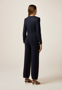 Navy denim crop-kut takki pitkähihaisilla, yhdistettynä leveälahkeisiin tummansinisiin housuihin. Ominaisuuksiin kuuluu muodollinen muotoilu ja kultaiset nappikoristeet.