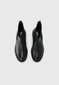 Scarpe nere slip-on con tomaia in pelle liscia, pannelli laterali elastici e suola in gomma testurizzata. Vista dall'alto. Nessun motivo o accessorio visibile.