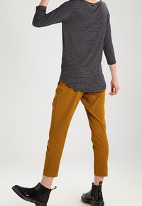 Schwarz-weißer gestreifter Langarm-Top mit abgerundetem Saum, kombiniert mit senfgelb tapered Hosen und glänzenden schwarzen Stiefeletten.