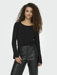 Maglietta nera a maniche lunghe con scollo ampio e polsini a coste, abbinata a pantaloni neri in finta pelle a vita alta con cuciture visibili.