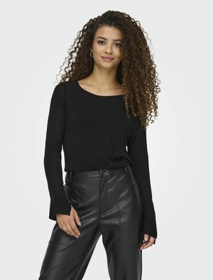 Maglietta nera a maniche lunghe con scollo ampio e polsini a coste, abbinata a pantaloni neri in finta pelle a vita alta con cuciture visibili.