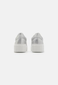 Metalliske sølv sneakers med en glatt tekstur, med en hvit, riftet gummisåle og rund tå, sett fra baksiden.