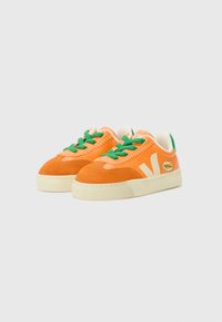 Sneaker in suede arancione con lacci verdi e suola crema. Presenta un logo laterale bianco e dettagli di cucitura a contrasto.