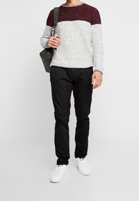 Pull en maille gris avec une partie supérieure bordeaux, associé à un pantalon noir et des baskets blanches. La tenue comprend un sac gris.