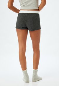 Grijze geribde shorts met een witte elastische tailleband, met een aansluitend ontwerp. Het model draagt lichtgrijze geribde sokken.