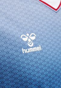 Zbliżenie na niebieską sportową koszulkę z subtelnym wzorem, białym logo „hummel” i kołnierzem w kształcie litery V z czerwonym wykończeniem.