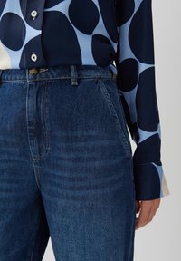 Marinblus med ljusblå mönster i rundade former, tillsammans med högmidjade mörk jeans i denim med strukturerade fickor och subtil sömnad.