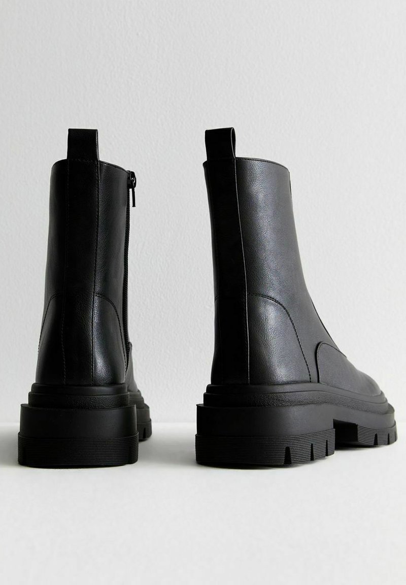 Bottes noires en cuir à la cheville avec une semelle épaisse, une fermeture éclair sur le côté et une languette d'enfilage. Texture lisse avec des accents cousus sur les côtés.