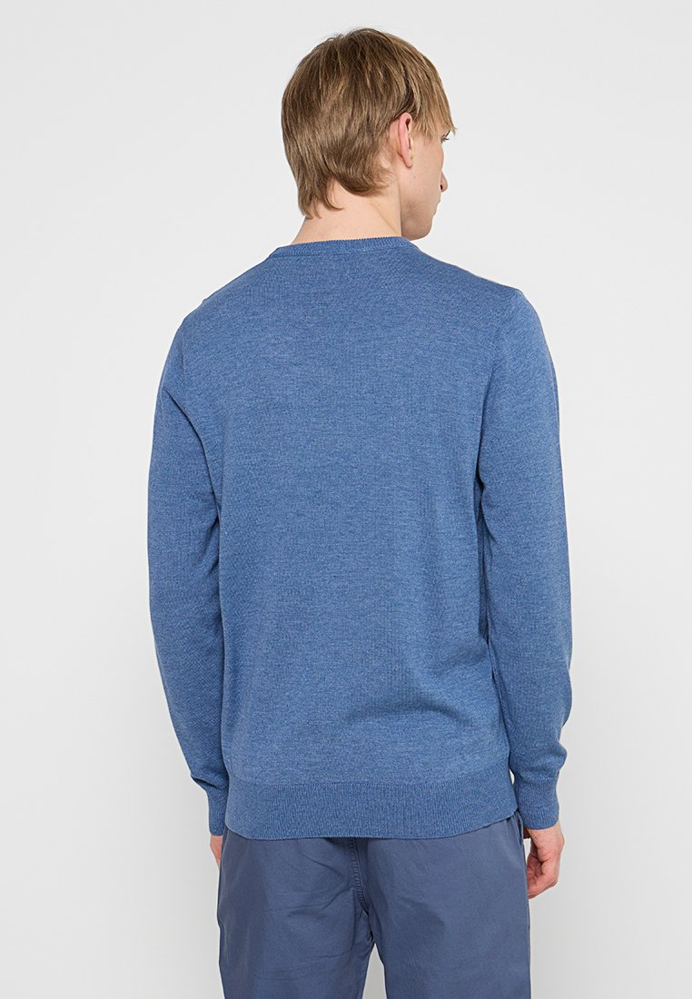 Pull en tricot bleu avec des manches longues, un col rond et un tissu texturé. La coupe est régulière, avec des poignets et un ourlet côtelés.