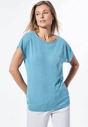 T-shirt bleu clair à manches courtes en tissu doux, avec un col rond et une coupe décontractée, associé à un pantalon blanc.