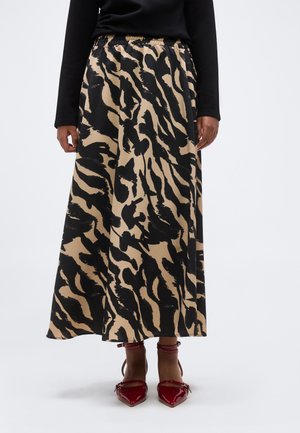 Γυναίκα που φοράει μπεζ και μαύρη ζέβρα midi φούστα, μαύρο μπλουζάκι με μακριά μανίκια και κόκκινα παπούτσια με λουράκι στον αστράγαλο και μυτερή μύτη.