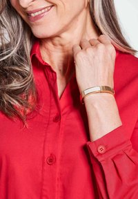 Rood hemd met knopen en opgerolde mouwen, met twee knopen op elke manchette. Een gouden armband siert de pols, met een gladde, gepolijste textuur.