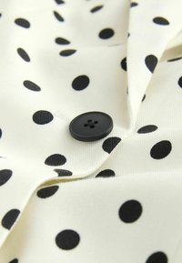 Tissu blanc à pois noirs avec un bouton noir à quatre trous cousu près d'un bord plié.