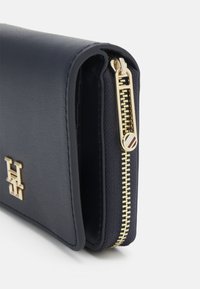 Portafoglio blu navy in materiale sintetico testurizzato; presenta elementi in metallo dorato per la cerniera e un accento con logo; forma compatta e rettangolare.