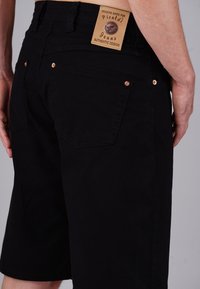 Black denim shorts with a straight cut, featuring copper rivets and back pocket stitching; includes a leather tag with brand name.
