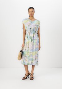 Blomstrete kortermet kjole med samlet midje, i pastellfarger. Komplementerer inkluderer en vevd veske og svarte stroppheler.